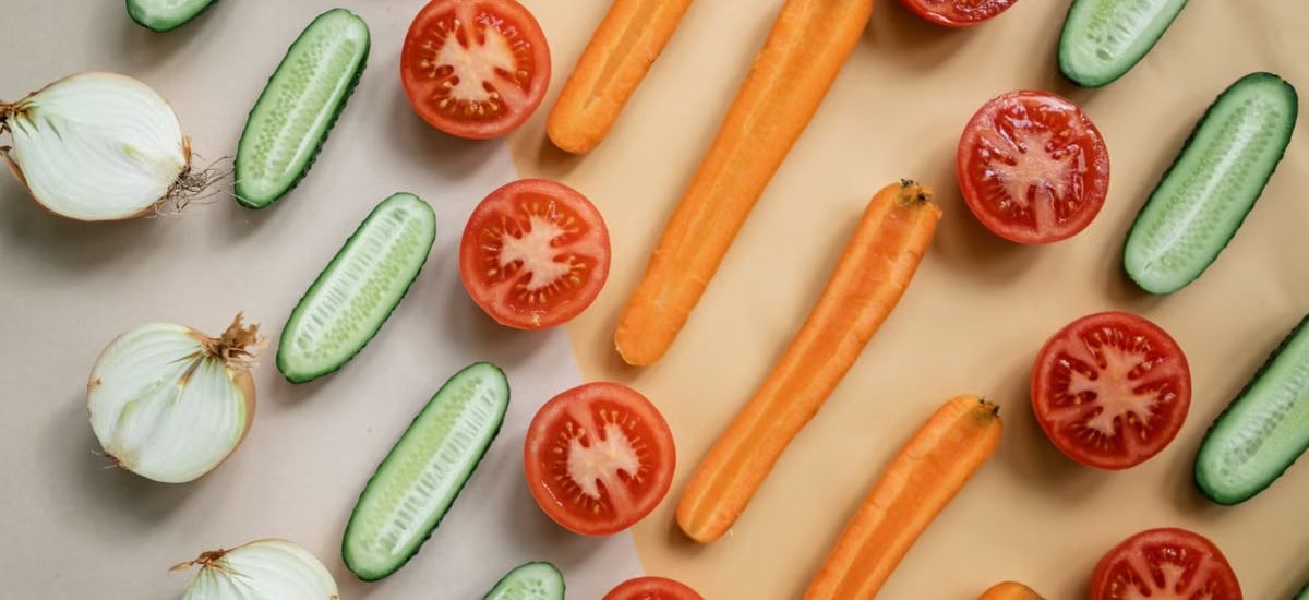 Top view of fresh sliced vegetables including carrots, cucumbers, onions, and tomatoes in a flat lay design.