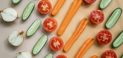 Top view of fresh sliced vegetables including carrots, cucumbers, onions, and tomatoes in a flat lay design.