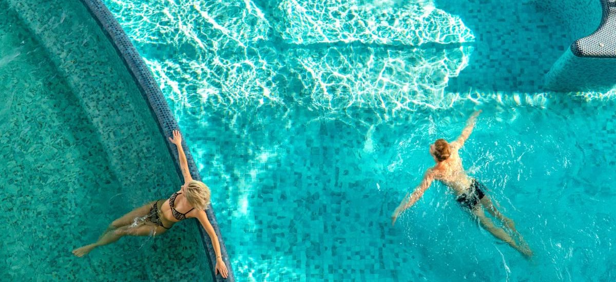 A couple relaxes in a bright swimming pool with clear water and light reflections.