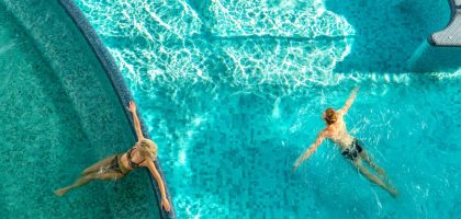 A couple relaxes in a bright swimming pool with clear water and light reflections.