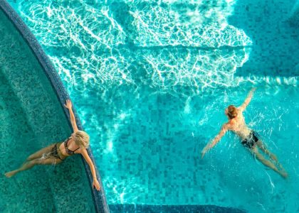 A couple relaxes in a bright swimming pool with clear water and light reflections.
